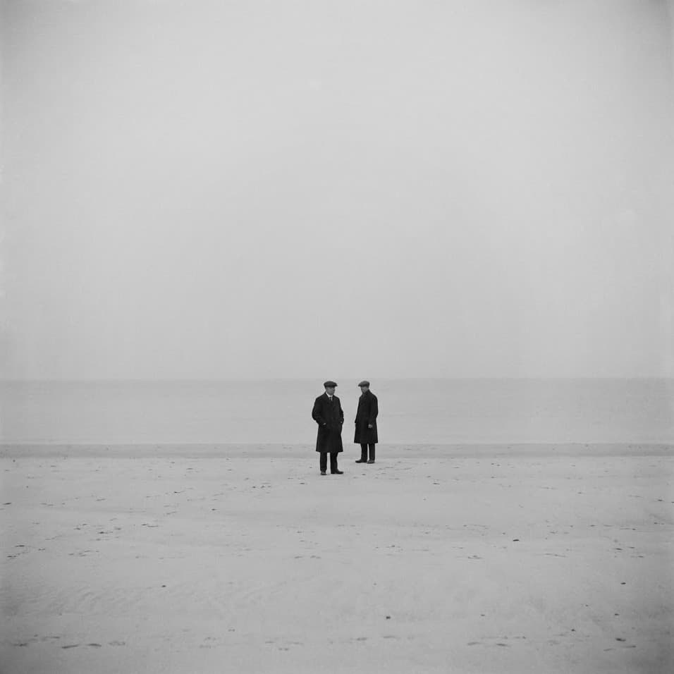 Two men in overcoats standing together on an empty beach